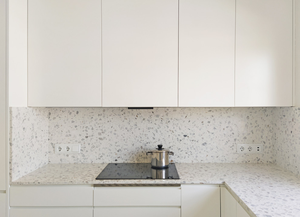 This is an example of a small modern u-shaped separate kitchen in Barcelona with an undermount sink, flat-panel cabinets, white cabinets, terrazzo benchtops, grey splashback, granite splashback, panelled appliances, terrazzo floors, no island, multi-coloured floor and grey benchtop.