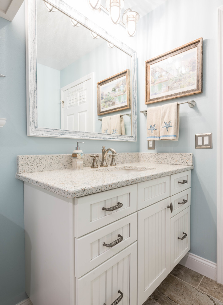 Photo of a large beach style 3/4 bathroom in Other with beaded inset cabinets, white cabinets, a corner shower, beige tile, porcelain tile, blue walls, porcelain floors, an undermount sink, recycled glass benchtops, beige floor and a hinged shower door.