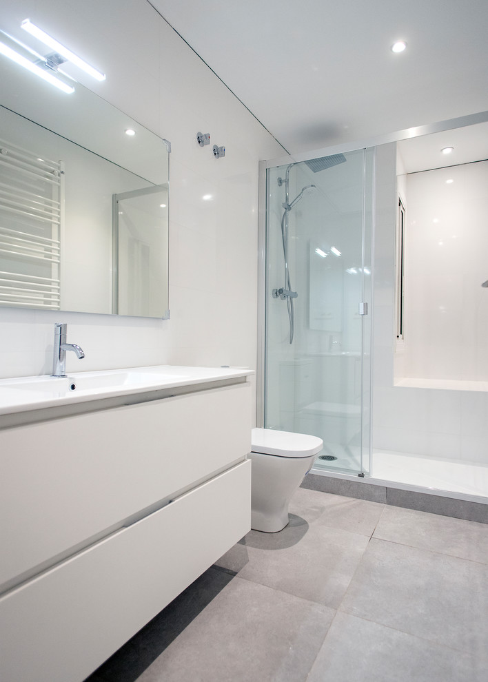 Photo of a mid-sized contemporary master bathroom in Barcelona with flat-panel cabinets, white cabinets, an alcove shower, a one-piece toilet, white tile, ceramic floors, grey floor, a sliding shower screen and white benchtops.