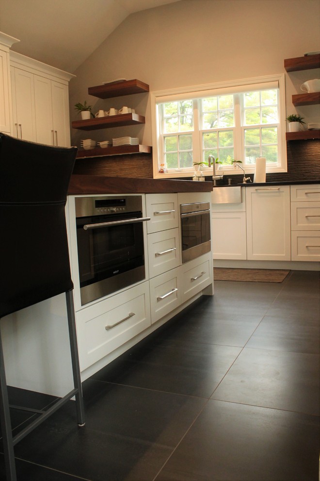 Inspiration for a mid-sized country u-shaped eat-in kitchen in Boston with a farmhouse sink, shaker cabinets, white cabinets, solid surface benchtops, black splashback, porcelain splashback, panelled appliances, ceramic floors, with island and black floor.