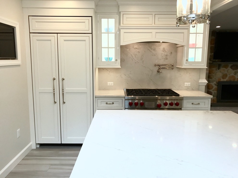 Mid-sized transitional u-shaped light wood floor and brown floor open concept kitchen photo with a farmhouse sink, recessed-panel cabinets, white cabinets, marble countertops, white backsplash, marble backsplash, stainless steel appliances and an island