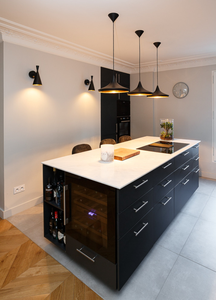 パリにあるお手頃価格の広いトラディショナルスタイルのおしゃれなキッチン (アンダーカウンターシンク、フラットパネル扉のキャビネット、黒いキャビネット、珪岩カウンター、白いキッチンパネル、クオーツストーンのキッチンパネル、パネルと同色の調理設備、セラミックタイルの床、グレーの床、白いキッチンカウンター) の写真