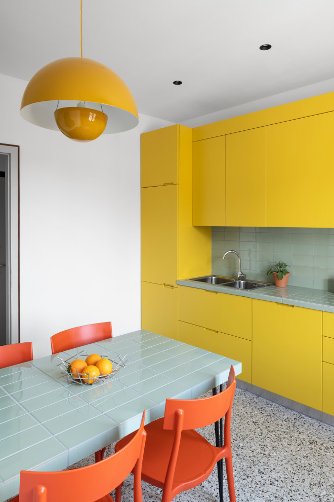 Design ideas for a mid-sized contemporary single-wall open plan kitchen in Venice with a double-bowl sink, flat-panel cabinets, yellow cabinets, tile benchtops, green splashback, porcelain splashback, panelled appliances, marble floors, multi-coloured floor, green benchtop and recessed.