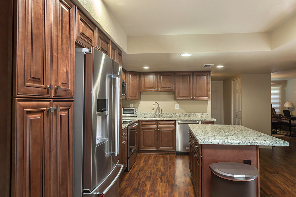 Mid-sized transitional l-shaped laminate floor and brown floor enclosed kitchen photo in Phoenix with an undermount sink, shaker cabinets, medium tone wood cabinets, granite countertops, multicolored backsplash, stone slab backsplash, stainless steel appliances and an island