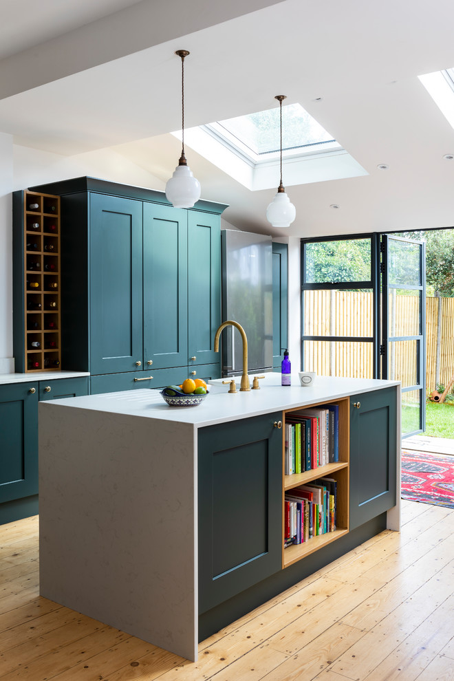 Design ideas for a mid-sized transitional galley eat-in kitchen in London with a drop-in sink, shaker cabinets, green cabinets, granite benchtops, white splashback, ceramic splashback, black appliances, light hardwood floors, with island, brown floor and white benchtop.