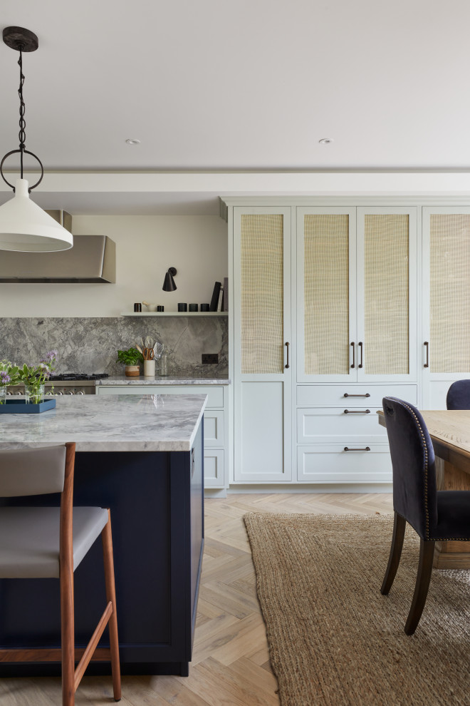 Medium sized classic galley kitchen/diner in London with shaker cabinets, blue cabinets, granite splashback, stainless steel appliances, light hardwood flooring, an island, grey worktops and feature lighting.