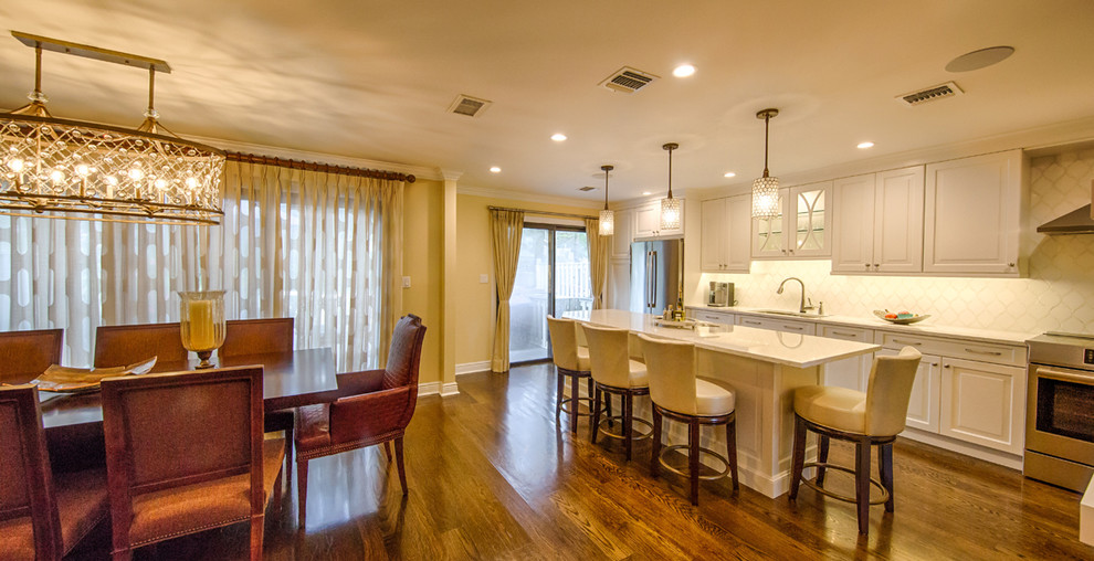 Inspiration for a mid-sized transitional single-wall dark wood floor and brown floor eat-in kitchen remodel in New York with an undermount sink, raised-panel cabinets, white cabinets, quartz countertops, white backsplash, glass tile backsplash, stainless steel appliances and an island