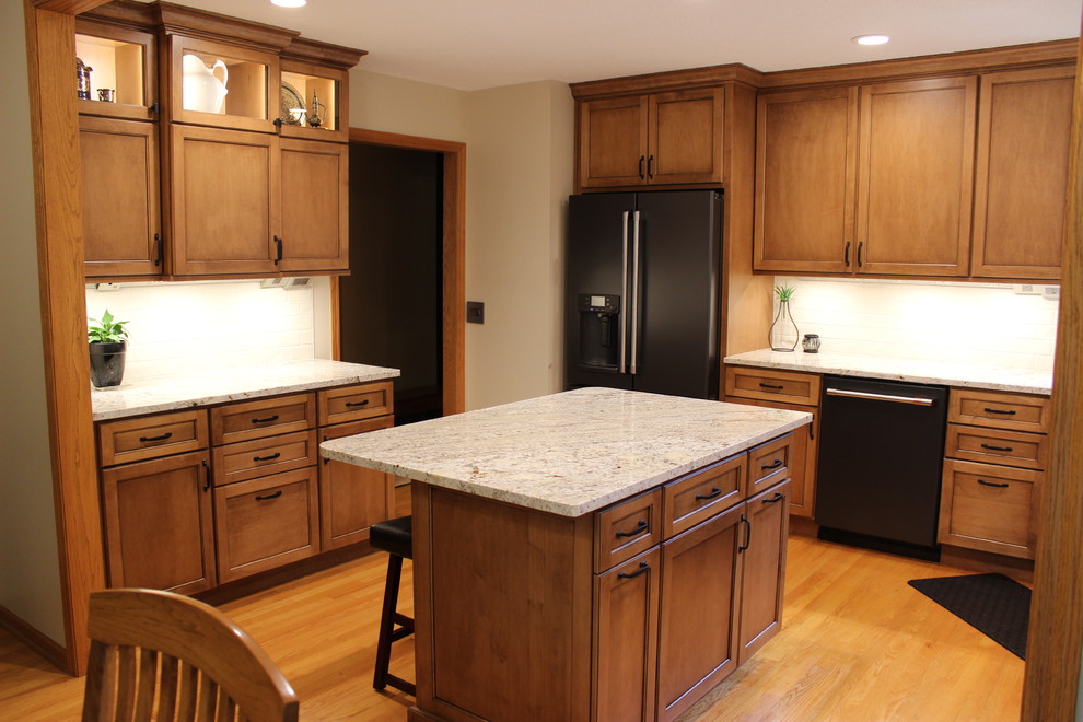 This is an example of a large transitional u-shaped eat-in kitchen in Other with an undermount sink, flat-panel cabinets, medium wood cabinets, granite benchtops, beige splashback, subway tile splashback, black appliances, light hardwood floors, with island, brown floor and beige benchtop.
