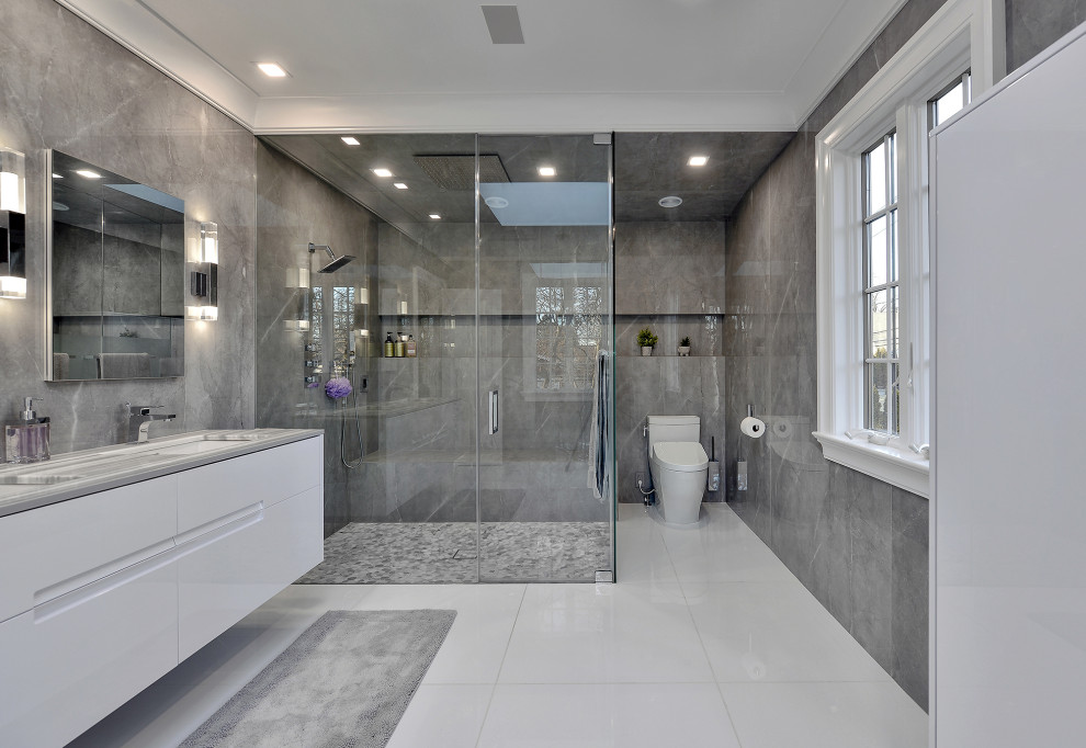 Bild på ett stort funkis grå grått en-suite badrum, med släta luckor, vita skåp, en kantlös dusch, en bidé, grå kakel, porslinskakel, grå väggar, marmorgolv, ett integrerad handfat, marmorbänkskiva, vitt golv och dusch med gångjärnsdörr