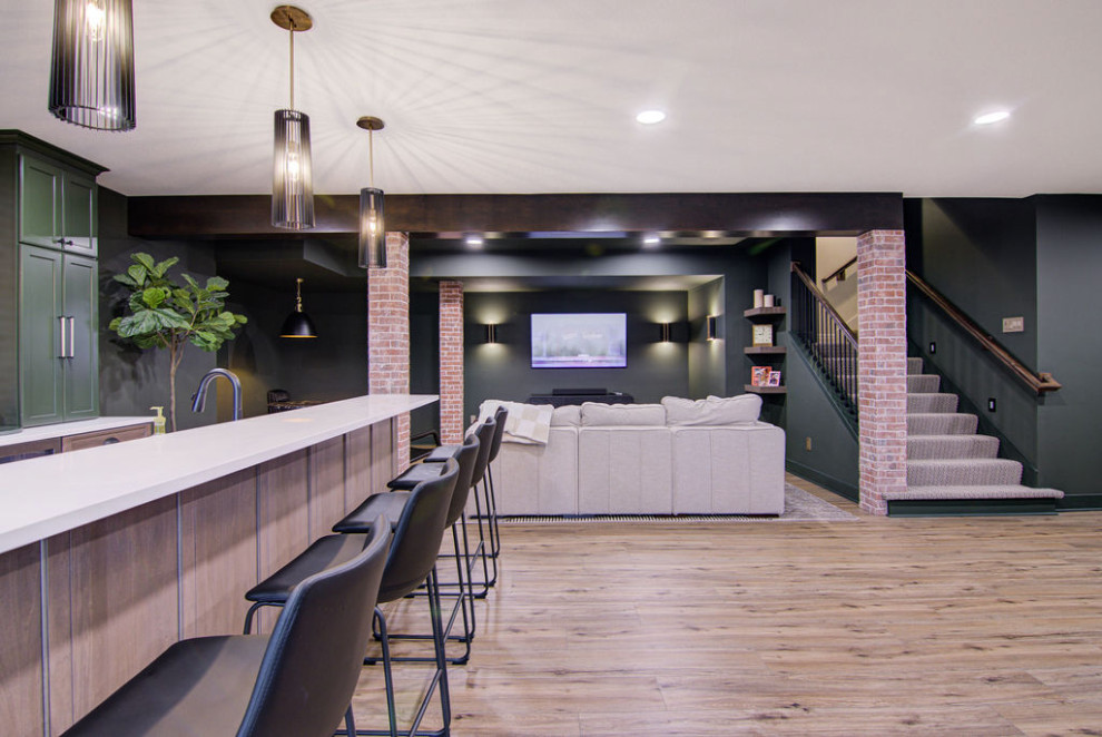 Aménagement d'un grand sous-sol moderne donnant sur l'extérieur avec un bar de salon, un mur vert, un sol en vinyl, poutres apparentes et un mur en parement de brique.