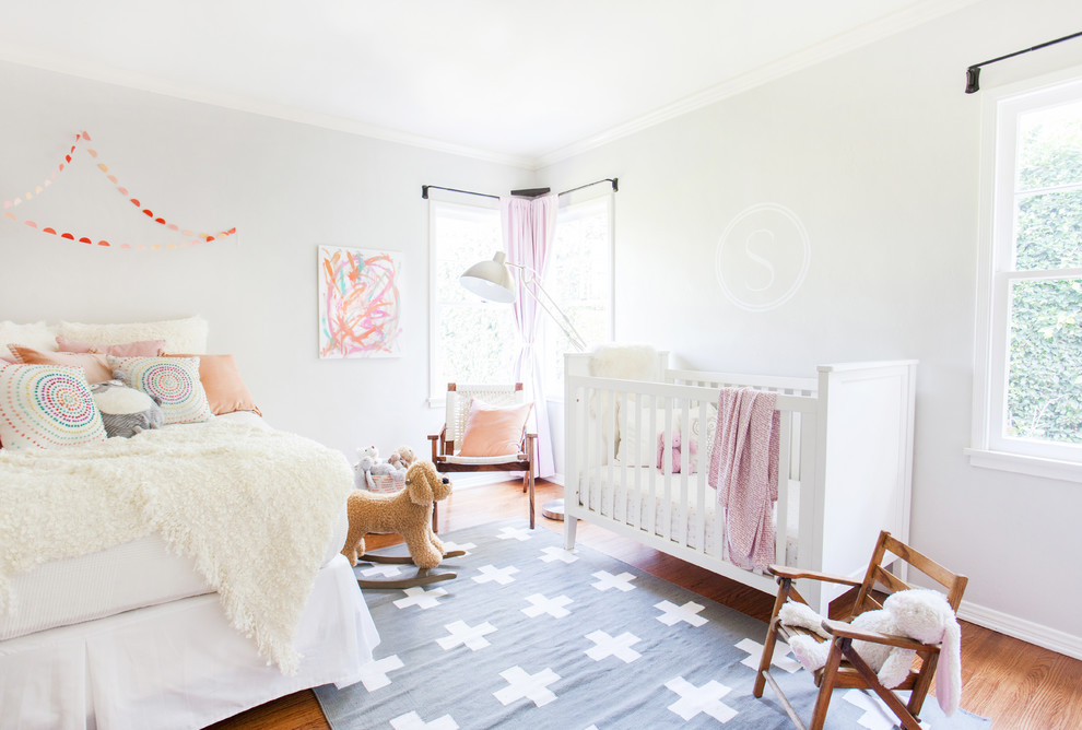 This is an example of a transitional nursery for girls in Los Angeles with grey walls and medium hardwood floors.