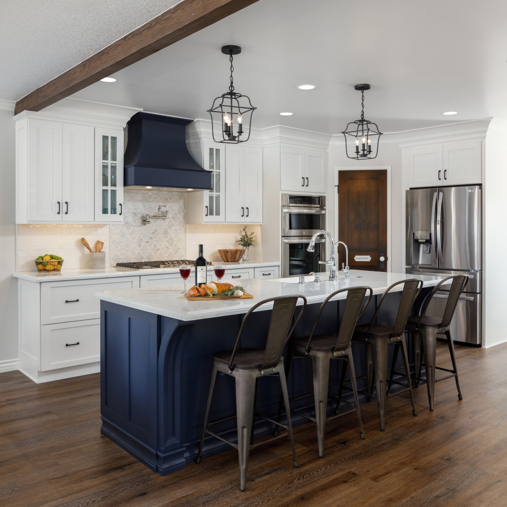 Inspiration for a large country single-wall eat-in kitchen in Los Angeles with a farmhouse sink, recessed-panel cabinets, white cabinets, quartz benchtops, white splashback, porcelain splashback, stainless steel appliances, vinyl floors, with island, brown floor, white benchtop and exposed beam.