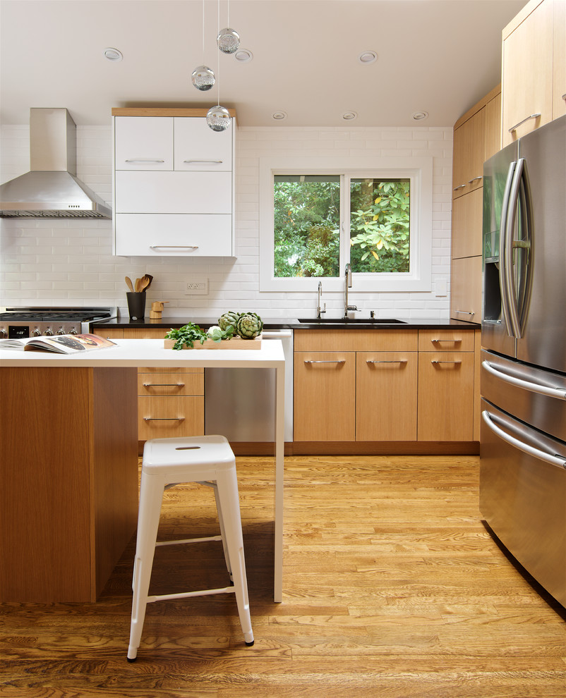 This is an example of a mid-sized contemporary l-shaped open plan kitchen in Seattle with flat-panel cabinets, quartz benchtops, white splashback, ceramic splashback, stainless steel appliances, with island, an undermount sink, medium wood cabinets, medium hardwood floors and brown floor.