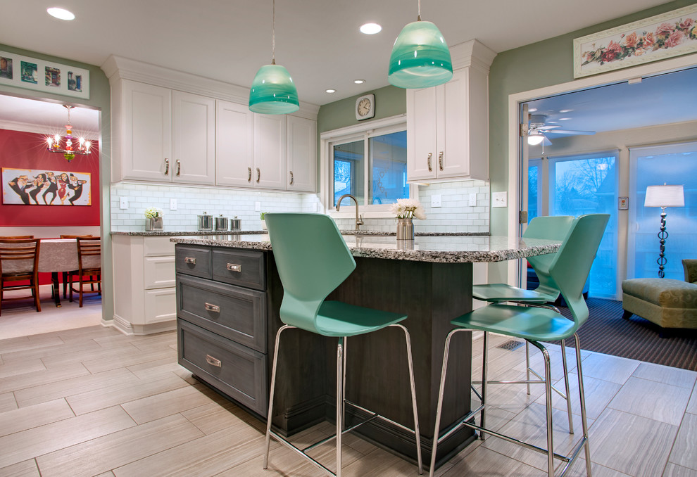 Example of a mid-sized transitional u-shaped porcelain tile kitchen pantry design with an undermount sink, recessed-panel cabinets, white cabinets, granite countertops, white backsplash, glass tile backsplash, stainless steel appliances and an island
