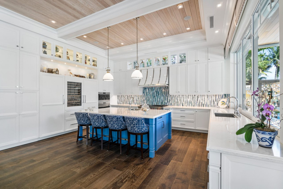 Example of a large beach style u-shaped medium tone wood floor, brown floor and coffered ceiling open concept kitchen design in Miami with an undermount sink, shaker cabinets, white cabinets, quartzite countertops, blue backsplash, glass tile backsplash, stainless steel appliances, an island and white countertops