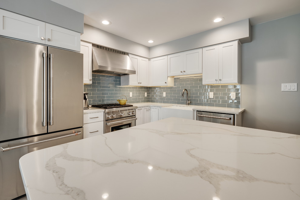 Small modern l-shaped separate kitchen in Philadelphia with a farmhouse sink, recessed-panel cabinets, white cabinets, quartz benchtops, blue splashback, glass tile splashback, stainless steel appliances, vinyl floors, with island, beige floor and white benchtop.