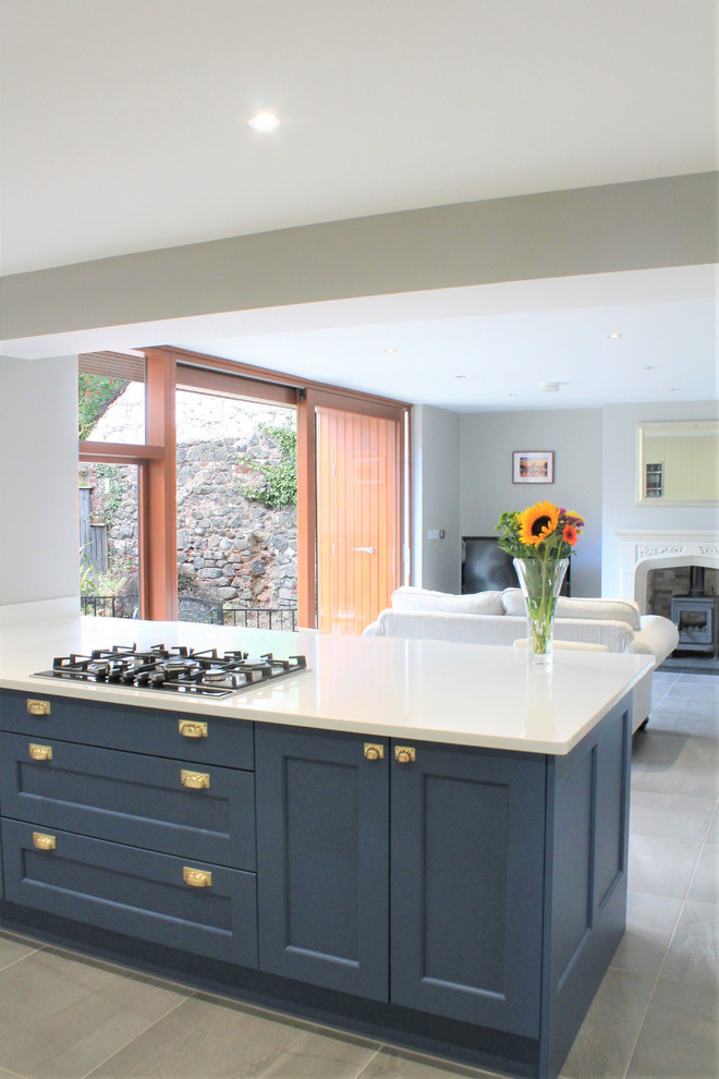 Medium sized modern galley open plan kitchen in Belfast with a built-in sink, shaker cabinets, blue cabinets, limestone worktops, white splashback, integrated appliances, porcelain flooring, a breakfast bar, grey floors and white worktops.