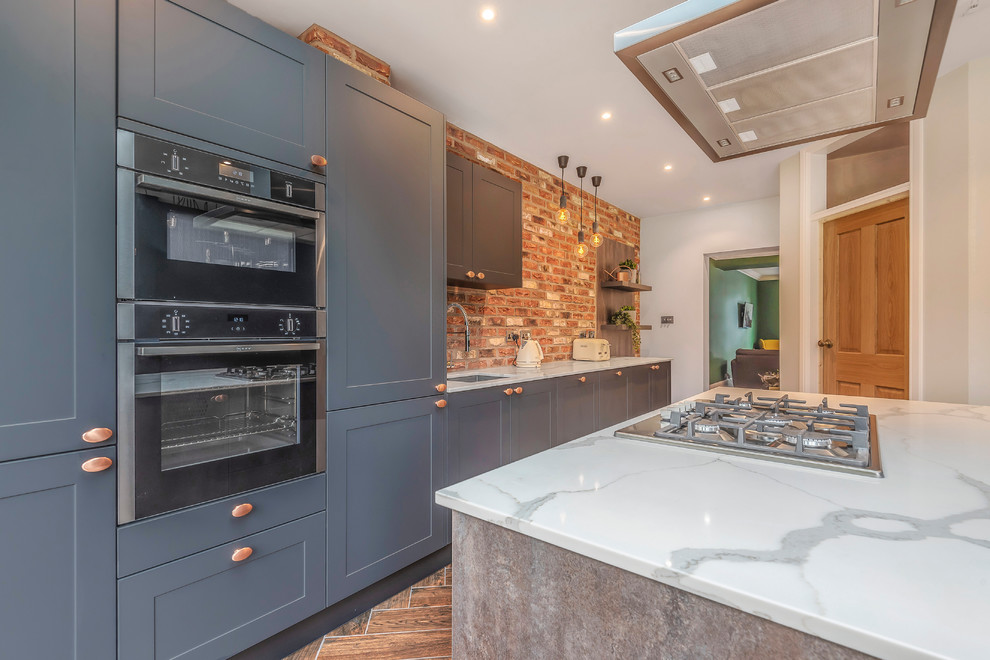 Industrial single-wall kitchen in Berkshire with shaker cabinets, blue cabinets, brick splashback, black appliances, with island and brown floor.