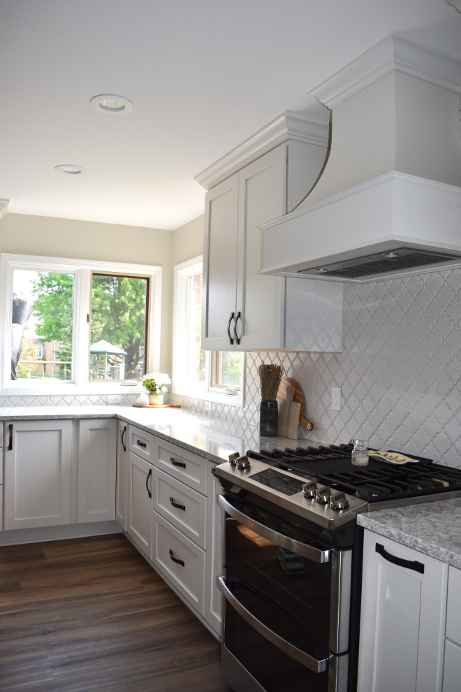 Large classic l-shaped kitchen/diner in Detroit with a submerged sink, shaker cabinets, white cabinets, engineered stone countertops, white splashback, ceramic splashback, stainless steel appliances, vinyl flooring, an island, brown floors and multicoloured worktops.