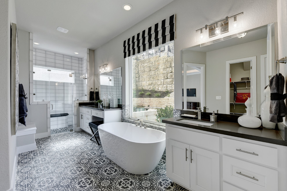 Inspiration for a transitional master bathroom in Austin with recessed-panel cabinets, white cabinets, a freestanding tub, white tile, grey walls, an undermount sink, multi-coloured floor and black benchtops.