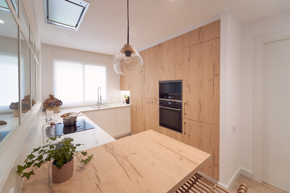 Photo of a mid-sized scandinavian u-shaped open plan kitchen in Barcelona with an undermount sink, light wood cabinets, white splashback, black appliances, laminate floors, a peninsula and white benchtop.