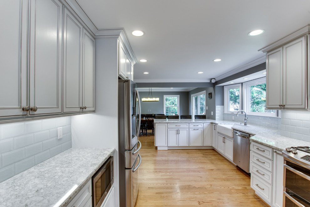 Inspiration for a large transitional kitchen in DC Metro with a farmhouse sink, recessed-panel cabinets, white cabinets, quartz benchtops, stainless steel appliances, medium hardwood floors and a peninsula.