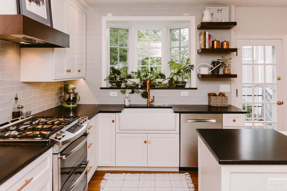 Inspiration for a mid-sized transitional u-shaped eat-in kitchen in Baltimore with a farmhouse sink, white cabinets, quartz benchtops, glass tile splashback, stainless steel appliances, medium hardwood floors, with island, brown floor, black benchtop, recessed-panel cabinets and blue splashback.