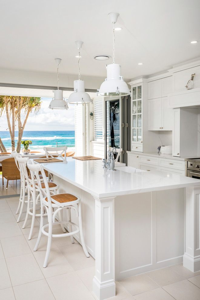 Large beach style galley eat-in kitchen in Gold Coast - Tweed with a farmhouse sink, white cabinets, marble benchtops, white splashback, marble splashback, stainless steel appliances, ceramic floors, with island, beige floor, white benchtop and recessed-panel cabinets.