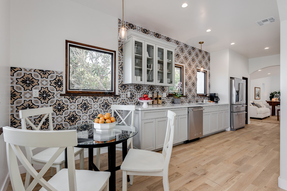 Design ideas for a mid-sized mediterranean galley eat-in kitchen in Los Angeles with recessed-panel cabinets, white cabinets, granite benchtops, multi-coloured splashback, no island, stainless steel appliances, light hardwood floors, an undermount sink, cement tile splashback and brown floor.