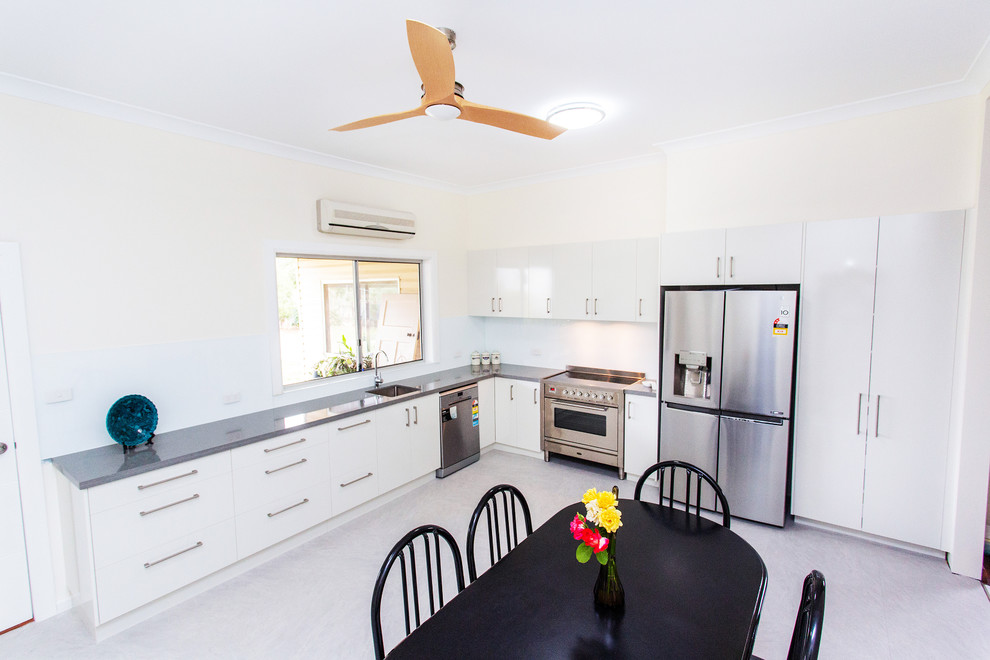 Photo of a mid-sized contemporary l-shaped eat-in kitchen in Other with an undermount sink, flat-panel cabinets, white cabinets, quartz benchtops, white splashback, glass sheet splashback, stainless steel appliances, linoleum floors, no island, grey floor and grey benchtop.