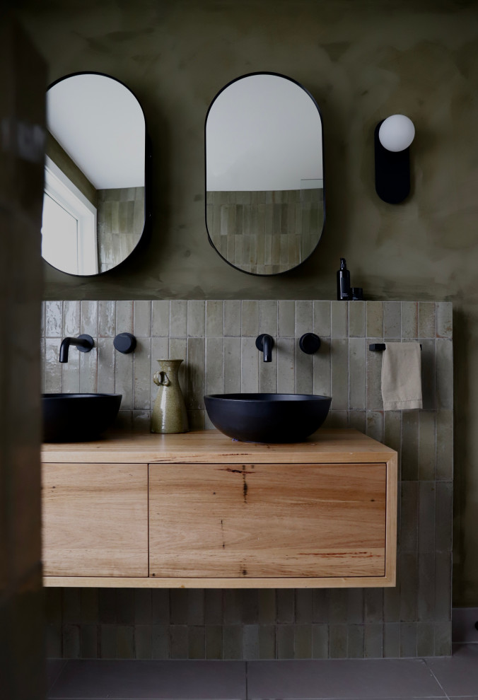 Modelo de cuarto de baño doble y flotante con puertas de armario de madera oscura, baldosas y/o azulejos verdes, paredes verdes y encimera de madera