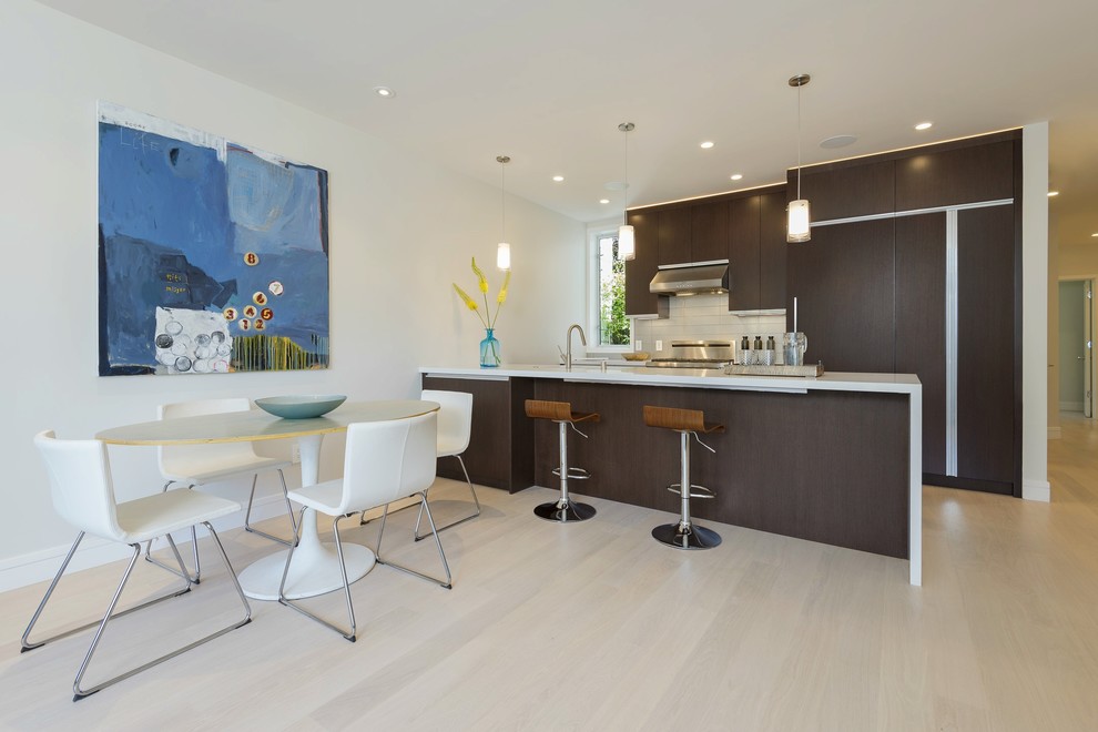 Photo of a mid-sized contemporary single-wall eat-in kitchen in San Francisco with an undermount sink, flat-panel cabinets, dark wood cabinets, solid surface benchtops, white splashback, ceramic splashback, panelled appliances, light hardwood floors and with island.