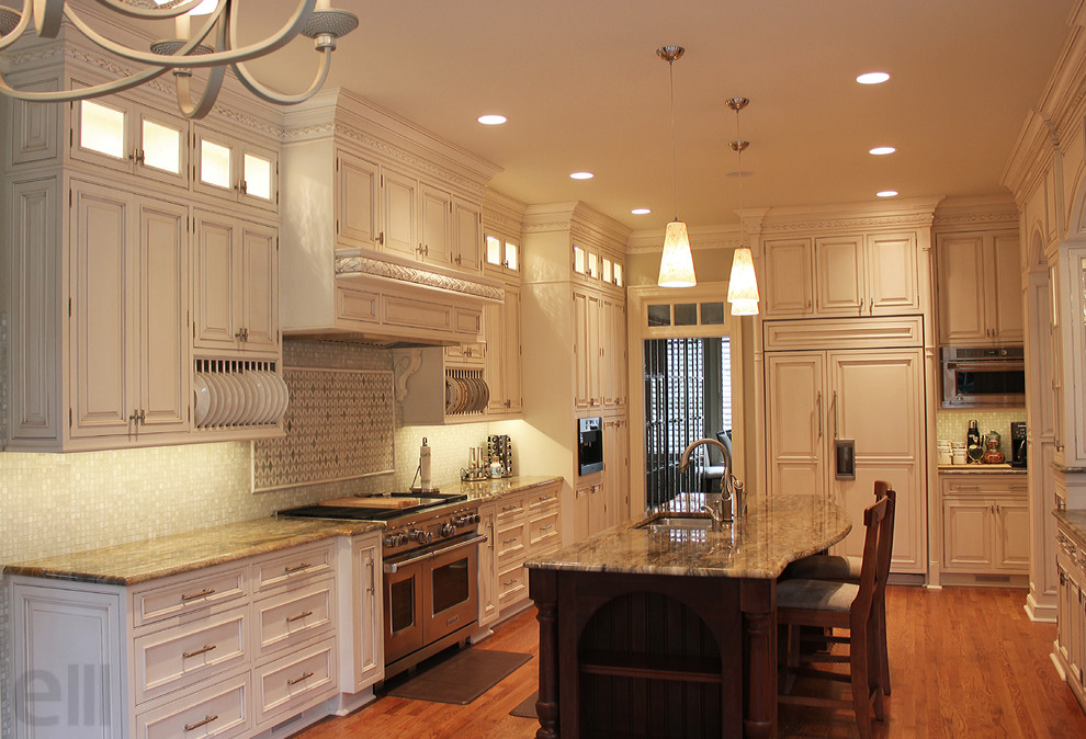 This is an example of a large traditional l-shaped eat-in kitchen in Charlotte with an undermount sink, beaded inset cabinets, white cabinets, granite benchtops, green splashback, mosaic tile splashback, panelled appliances and light hardwood floors.