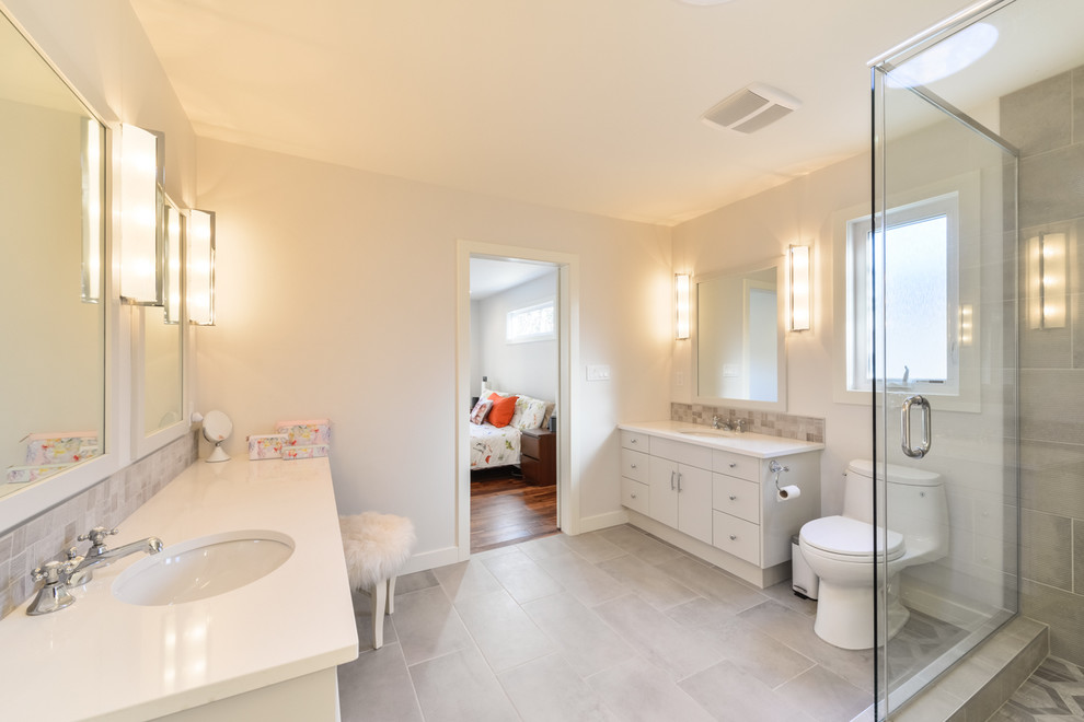 Inspiration for a mid-sized contemporary master bathroom in Orange County with flat-panel cabinets, white cabinets, a freestanding tub, an alcove shower, gray tile, porcelain tile, white walls, porcelain floors, an undermount sink, solid surface benchtops, grey floor and a hinged shower door.