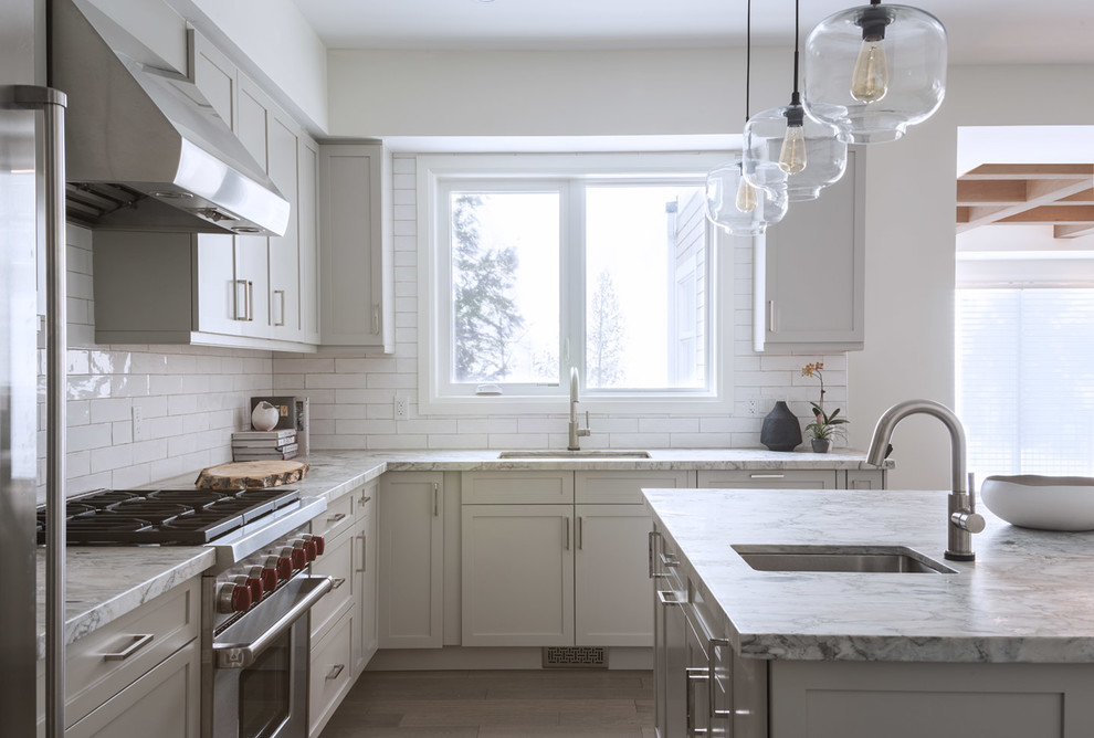 This is an example of a small contemporary l-shaped open plan kitchen in Toronto with a single-bowl sink, shaker cabinets, grey cabinets, quartzite benchtops, white splashback, subway tile splashback, stainless steel appliances, light hardwood floors, with island and white benchtop.