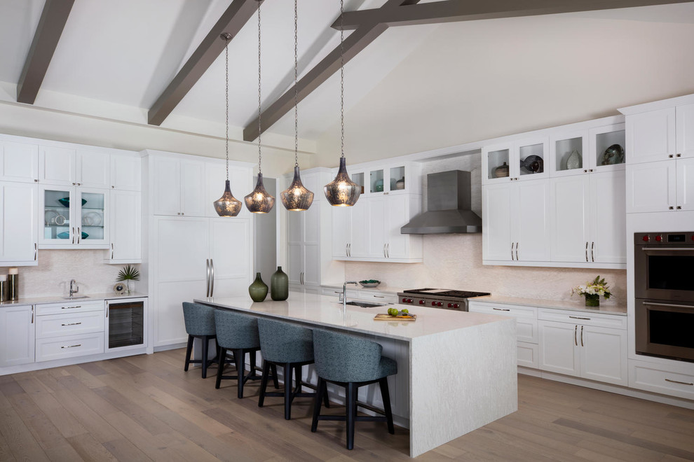 Design ideas for a large transitional l-shaped open plan kitchen in Miami with a drop-in sink, white cabinets, granite benchtops, white splashback, stone slab splashback, panelled appliances, light hardwood floors, with island, brown floor and white benchtop.