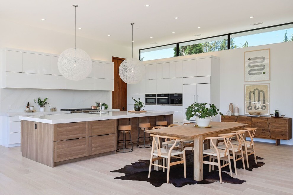 Contemporary l-shaped eat-in kitchen in San Francisco with an undermount sink, flat-panel cabinets, white cabinets, white splashback, stainless steel appliances, light hardwood floors, with island, beige floor and white benchtop.