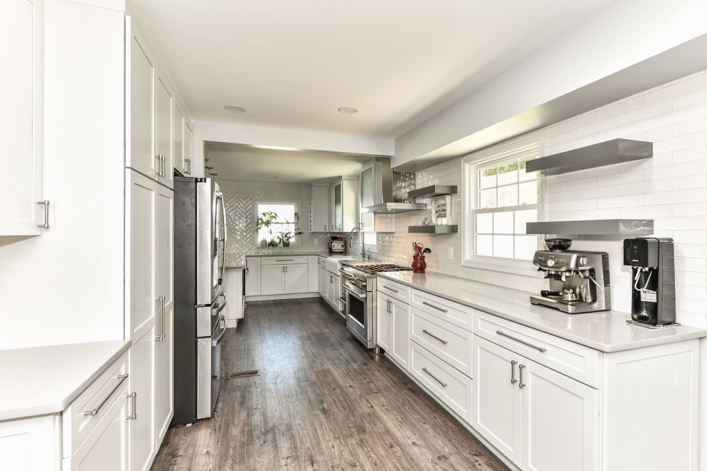 Design ideas for a large modern galley eat-in kitchen in DC Metro with a farmhouse sink, shaker cabinets, white cabinets, quartzite benchtops, white splashback, porcelain splashback, stainless steel appliances, vinyl floors, with island, brown floor and grey benchtop.
