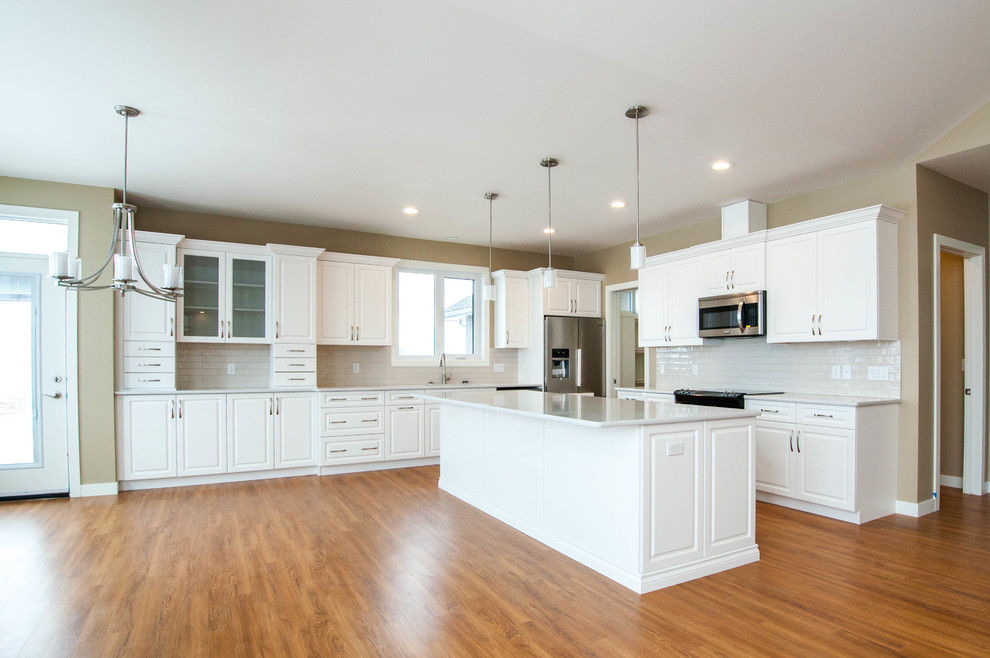 Inspiration for a huge transitional l-shaped vinyl floor and brown floor eat-in kitchen remodel in Calgary with an undermount sink, raised-panel cabinets, white cabinets, quartz countertops, white backsplash, subway tile backsplash, stainless steel appliances and an island
