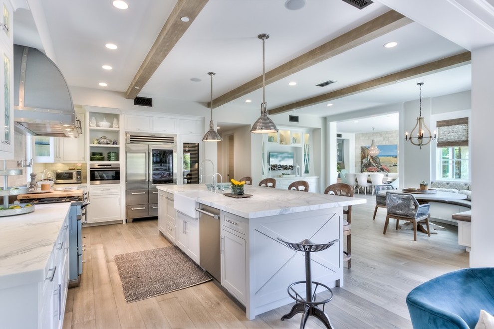 This is an example of a large country l-shaped open plan kitchen in Orange County with a farmhouse sink, recessed-panel cabinets, white cabinets, marble benchtops, white splashback, subway tile splashback, stainless steel appliances, light hardwood floors and with island.