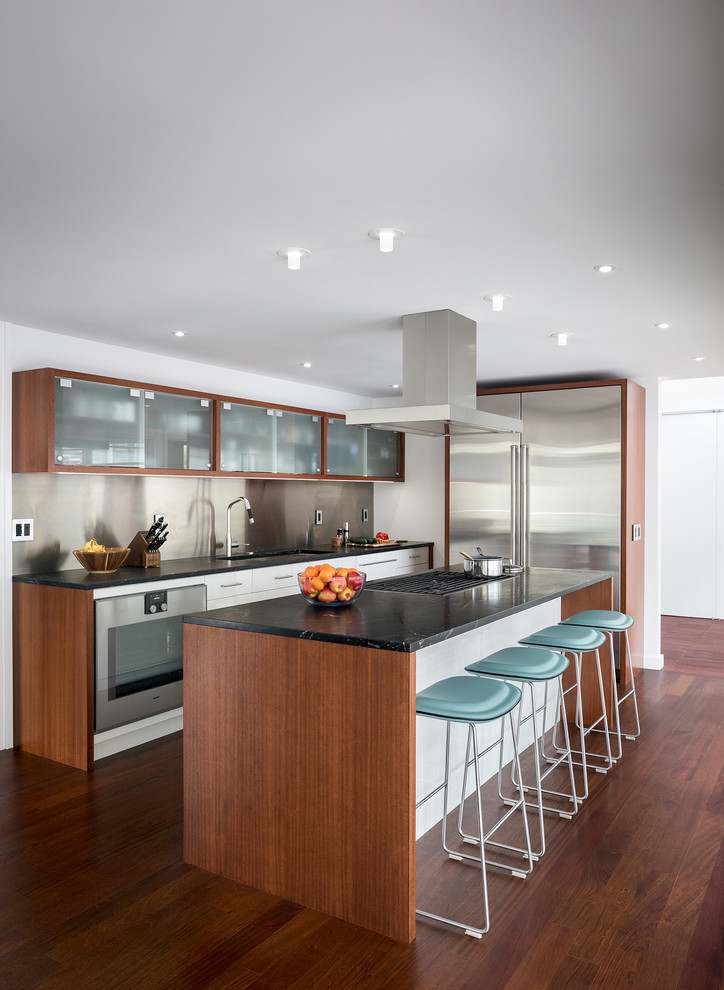 This is an example of a contemporary u-shaped kitchen in New York with white cabinets, metallic splashback, stainless steel appliances, dark hardwood floors, with island and brown floor.