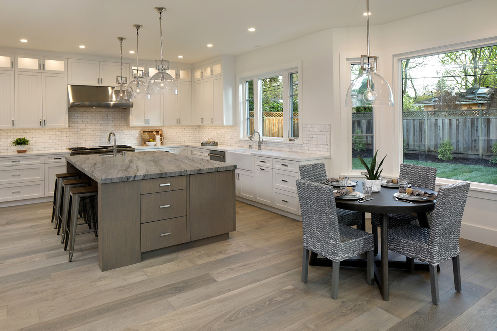 This is an example of a large country u-shaped open plan kitchen in San Francisco with a farmhouse sink, white cabinets, stainless steel appliances, medium hardwood floors, with island, grey floor, recessed-panel cabinets, quartzite benchtops, white splashback, marble splashback and white benchtop.