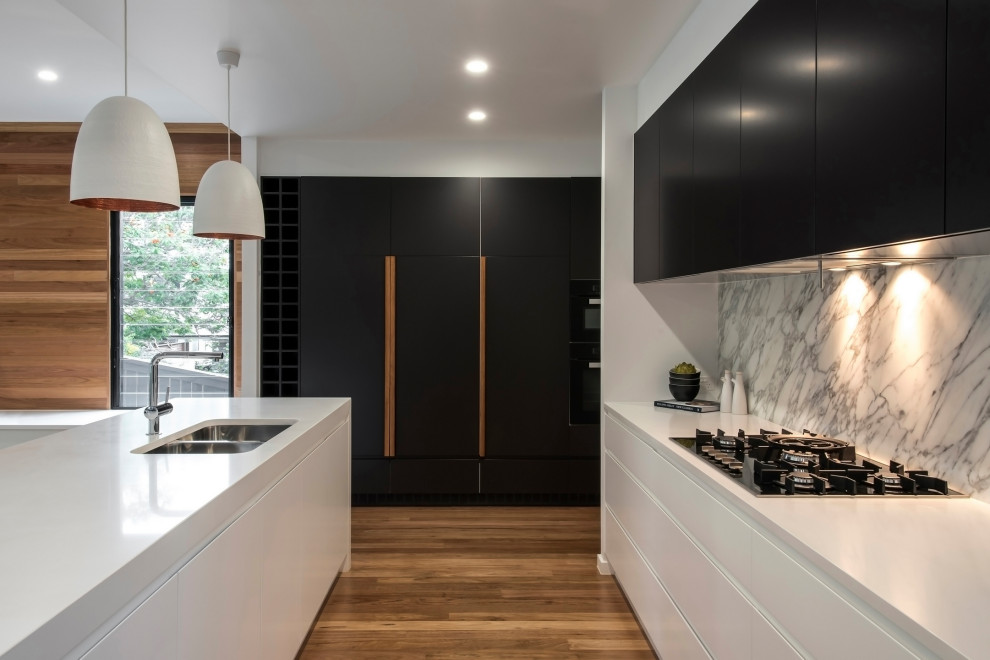 Contemporary galley kitchen with an undermount sink, black cabinets, grey splashback, marble splashback, medium hardwood floors, with island and white benchtop.