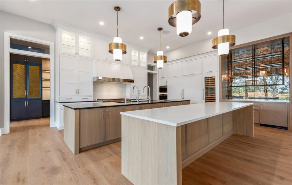 Example of a huge transitional single-wall light wood floor, brown floor and exposed beam kitchen design in Chicago with an undermount sink, shaker cabinets, light wood cabinets, quartz countertops, white backsplash, quartz backsplash, paneled appliances, two islands and white countertops