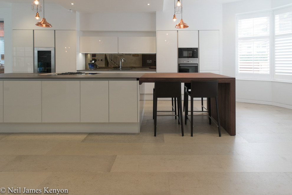 Design ideas for a mid-sized single-wall open plan kitchen in London with a drop-in sink, flat-panel cabinets, white cabinets, wood benchtops, metallic splashback, window splashback, stainless steel appliances, ceramic floors and with island.