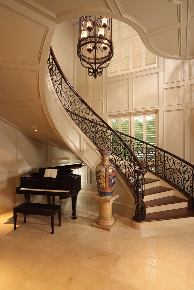 This is an example of a large traditional wood curved staircase in Houston with marble risers and metal railing.