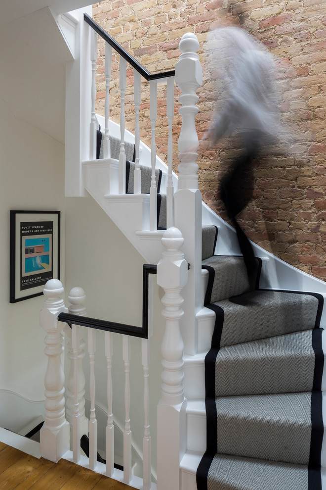 Photo of a mid-sized contemporary carpeted curved staircase in London with wood risers and wood railing.
