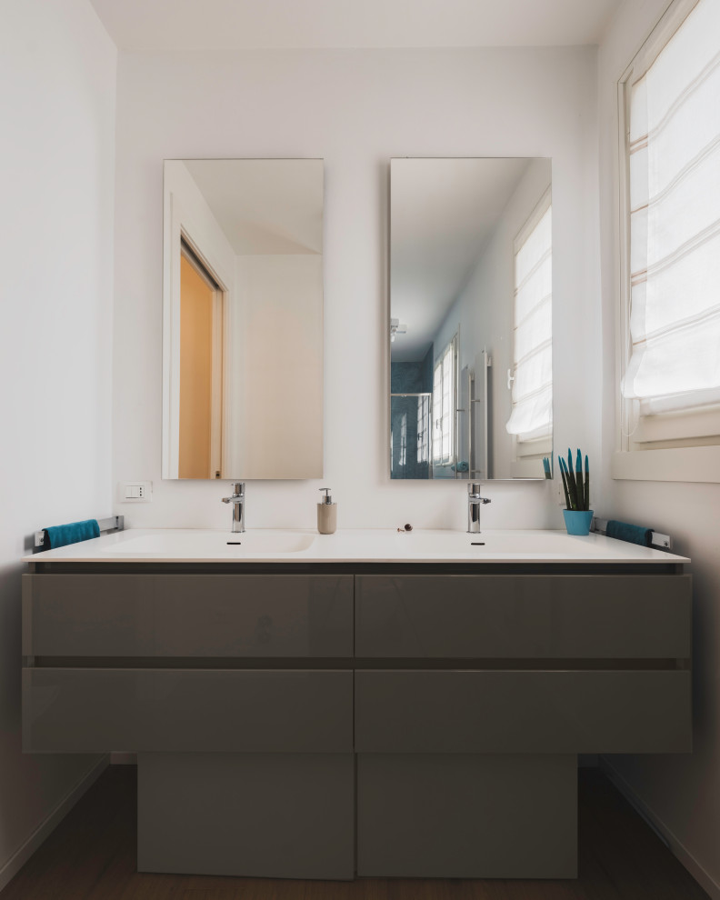 This is an example of a mid-sized contemporary 3/4 bathroom in Milan with flat-panel cabinets, grey cabinets, an alcove shower, a two-piece toilet, blue tile, porcelain tile, white walls, light hardwood floors, a drop-in sink, solid surface benchtops, beige floor, a sliding shower screen, white benchtops, a double vanity and a floating vanity.