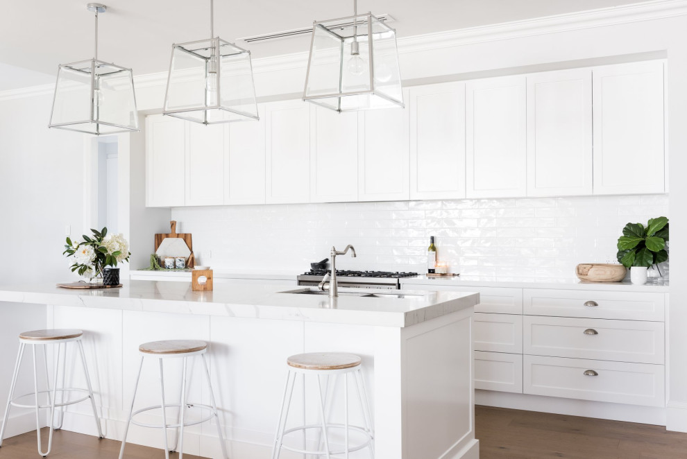 Country galley kitchen in Sydney with an undermount sink, shaker cabinets, white cabinets, white splashback, subway tile splashback, stainless steel appliances, medium hardwood floors, with island, brown floor and white benchtop.