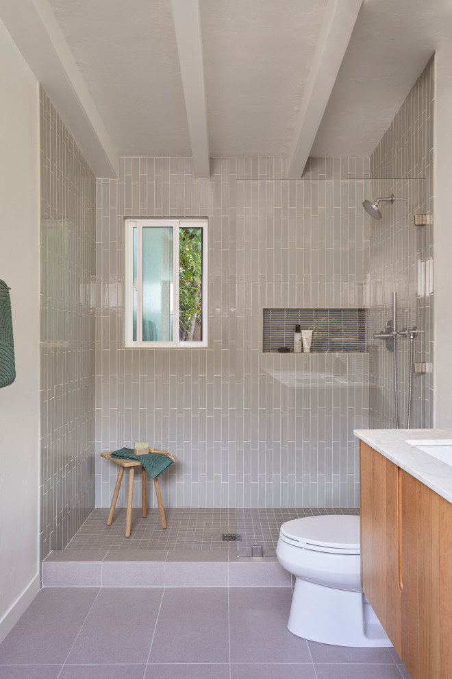 This is an example of a mid-sized midcentury master bathroom in San Francisco with flat-panel cabinets, brown cabinets, an alcove shower, a two-piece toilet, gray tile, ceramic tile, white walls, porcelain floors, an undermount sink, marble benchtops, grey floor, an open shower, white benchtops, a niche, a double vanity, a floating vanity and exposed beam.